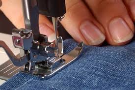 Close-up of a sewing machine stitching a hem in denim fabric.